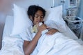Mixed race sick girl asleep in hospital bed wearing fingertip pulse oximeter and holding teddy bear Royalty Free Stock Photo