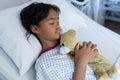 Mixed race sick girl holding teddy bear lying asleep in bed in a hospital ward Royalty Free Stock Photo