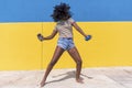 Mixed race smiling black woman portrait with big afro curly hair against blue and yellow wall dancing while holding a smartphone Royalty Free Stock Photo