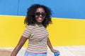 Mixed race smiling black woman portrait with big afro curly hair against blue and yellow wall dancing while holding a smartphone Royalty Free Stock Photo