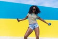 Mixed race smiling black woman portrait with big afro curly hair against blue and yellow wall dancing while holding a smartphone Royalty Free Stock Photo