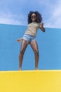 Mixed race smiling black woman portrait with big afro curly hair against blue and yellow wall dancing while holding a smartphone Royalty Free Stock Photo