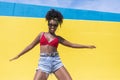 Mixed race smiling black woman portrait with big afro curly hair against blue and yellow wall dancing while holding a smartphone Royalty Free Stock Photo