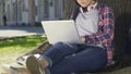 Mixed-race student doing her diploma project sitting with laptop openair