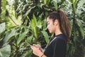 Mixed race teenage woman with earphones listening to the music, against green trees tropical background. Royalty Free Stock Photo