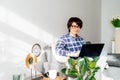 Mixed race woman in eye glasses using laptop at home sitting on soft couch. Cozy workspace in modern interior with green