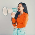 Mixed race woman isolated against grey studio background with copyspace and using megaphone. Young hispanic standing