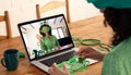 Mixed race woman making st patrick's day video call to waving female friend on laptop at home Royalty Free Stock Photo