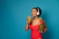 Mixed race woman in red swimsuit holds pineapple with blank red card and drinks exotic cocktail while enjoying music with Royalty Free Stock Photo