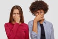 Mixed race women hold breath from unpleasant smell, cover noses, frown faces in dicontent, notice spoiled product, look Royalty Free Stock Photo