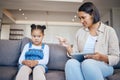 Mixed race woman pointing to scold and discipline her little daughter about internet use on digital tablet at home
