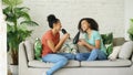 Mixed race young funny girls dance singing with hairdryer and comb sitting on sofa. Sisters having fun leisure in living Royalty Free Stock Photo