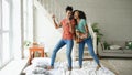 Mixed race young funny girls dance singing with hairdryer and playing acoustic guitar on a bed. Sisters having fun Royalty Free Stock Photo