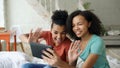 Cheerful mixed race young funny girls talking online video chat on tablet computer with their friends at home Royalty Free Stock Photo