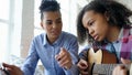 Mixed race young woman with tablet computer sitting on bed teaching her teenage sister to play acoustic guitar at home Royalty Free Stock Photo