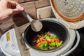 Mixed set of vegetarian vegetables in a white multicooker is stirred with a kitchen plastic scraper. Onions, peppers, Royalty Free Stock Photo