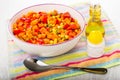 Mixed pepper, carrot, green peas, corn in ceramic bowl, bottle of vegetable oil, salt, spoon on napkin on table