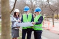 Mixed team of senior men and young female architects or business partners looking at building plans on a construction site