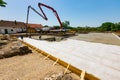 Mixer truck on the site, worker holds pump to pours concrete into building foundation, riggers are leveling it