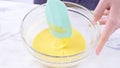Mixing egg yolk into cake batter with green rubber spatula mixer tool stirring until smooth and blend well in a glass bowl, close