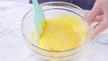 Mixing egg yolk into cake batter with green rubber spatula mixer tool stirring until smooth and blend well in a glass bowl, close