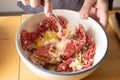 Mixing minced meat and other ingredients with a fork in a bowl, preparation to cook meatballs