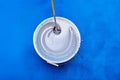 Mixing White Paint in Bucket Against Vivid Blue Background. Royalty Free Stock Photo