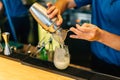 Mixologist making cocktail with Shaker, Double Size Jiggers and drinking glass with ice cube on cocktail counter bar