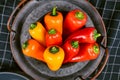 Mixture of chilli shaped red, orange and yellow capsicums pepper vegetables in bowl on dark background