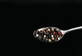 A mixture of pepper varieties with peas in a spoon on the black background. Heap of various pepper. Mix of red, black