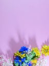 A mixture pf blue and yellow silk flowers forming a lower border on vertical pink background.