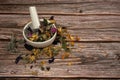 A mixture of various medicinal herbs in a porcelain mortar with a pestle on a wooden background.