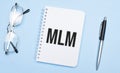 mlm words in white notepad, pen and glasses on blue background. Concept Royalty Free Stock Photo