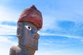 Moai statue with eyes near the Hanga Roa village on Easter Island, against a blue sky covered by white clouds.