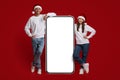 Mobile Ad. Happy Couple Wearing Santa Hats Leaning At Big Blank Smartphone Royalty Free Stock Photo