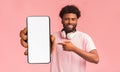 Mobile advertisement. Happy black man pointing at smartphone with empty white screen on pink background, mockup