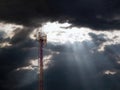 Mobile antenna, high metal tower against a dramatic sky with the rays of the sun breaking through the clouds Royalty Free Stock Photo