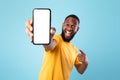 Mobile app advertisement. Excited black man pointing at smartphone with empty screen, mockup. Space for ad or website