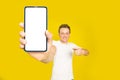 Mobile app advertising handsome blond man pointing at giant smartphone with white empty screen, wearing white t-shirt Royalty Free Stock Photo