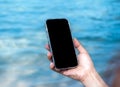 Mobile beach phone with empty screen. Mockup image of black blank desktop screen in hand holding mobile smart phone on the blue. Royalty Free Stock Photo