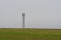 Mobile cell tower antenna mast providing mobile internet connection for rural area standing on empty barren field on grey overcast