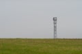 Mobile cell tower antenna mast providing mobile internet connection for rural area standing on empty barren field on grey overcast