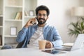 Mobile Communication. Handsome Young Indian Man Talking On Cellphone And Drinking Coffee Royalty Free Stock Photo