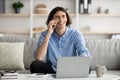 Mobile communication. Happy male freelancer talking on cellphone and working on laptop, sitting on sofa at home Royalty Free Stock Photo