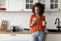 Mobile Communication. Young Black Woman Using Smartphone And Drinking Coffee In Kitchen Royalty Free Stock Photo