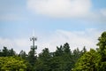 Mobile communications tower with antennas on top, showing above a forest tree line, sky and clouds in the background Royalty Free Stock Photo