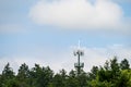 Mobile communications tower with antennas on top, showing above a forest tree line, sky and clouds in the background Royalty Free Stock Photo