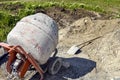 Mobile concrete mixer on background of pile of gravel. Preparatory work for preparation of concrete mass. Shadow from construction