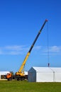 Mobile crane with yellow arrow lift a heavy load against the blue sky, construction of an industrial facility, houses, buildings