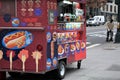 Red hot dog street food cart with worker sweeping sidewalk